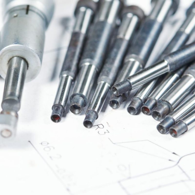 Close-up of a micrometer and several precision metal rods on a technical drawing paper.