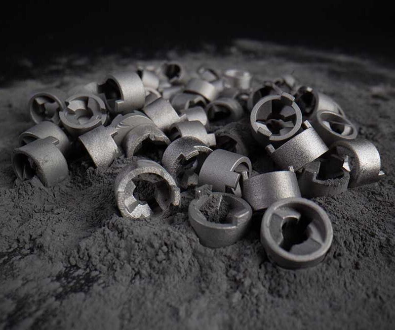 A pile of small metallic parts sits on a surface covered with fine gray dust.
