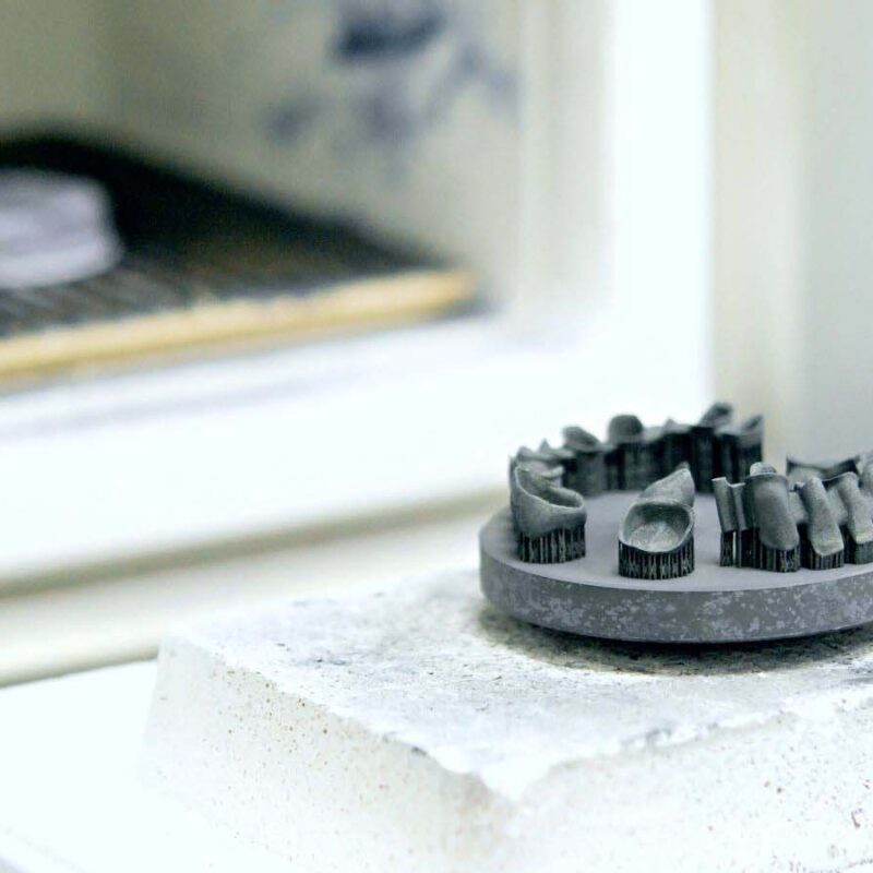 A 3D-printed dental model on a stone platform, illuminated by the glow of an open furnace, showcases the precision of Metal 3D Printing.