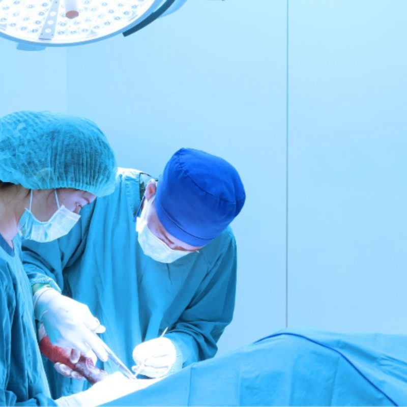 Two surgeons in scrubs and masks perform an operation under bright surgical lights in an operating room.