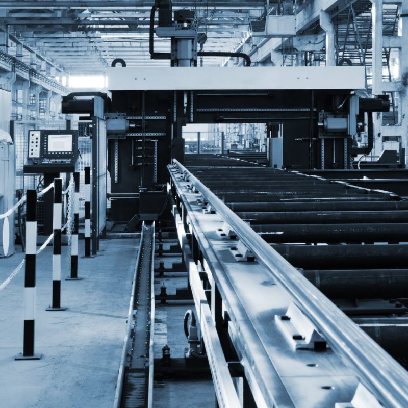 A modern industrial factory with large machinery and conveyor belts handling production of steel pipes, shown in a monochrome blue tone.