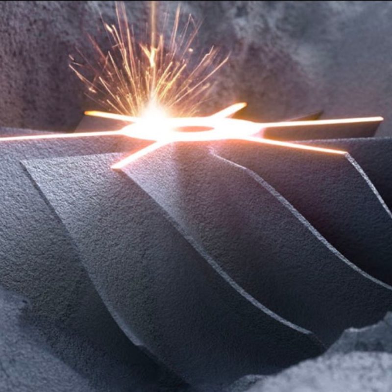 A close-up image of a lit sparkler placed on a gray, textured surface, emitting a bright light and sparks.