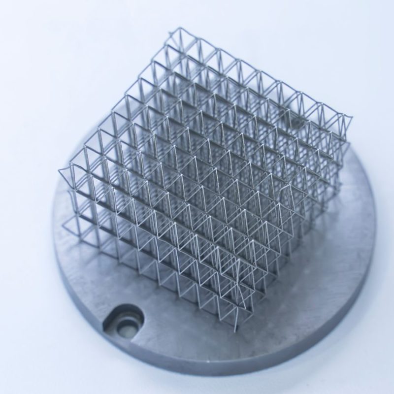 Metal jetting mesh sculpture mounted on a circular base, featuring a complex grid structure, displayed against a plain white background.