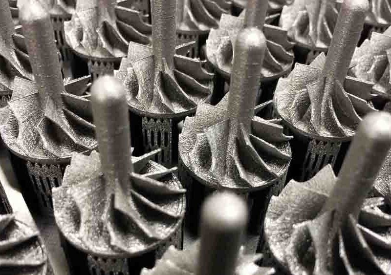 Close-up view of a group of machined metal turbine blades arranged in rows, showcasing intricate engineering details and symmetrical design, with careful printing on metal surfaces enhancing the precision and functionality.