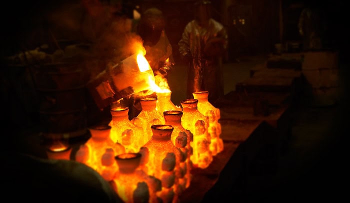 Workers in protective gear pour molten metal into molds, creating a glowing effect in a dimly lit foundry, reminiscent of the advanced techniques that have driven down the cost of 3D printing.