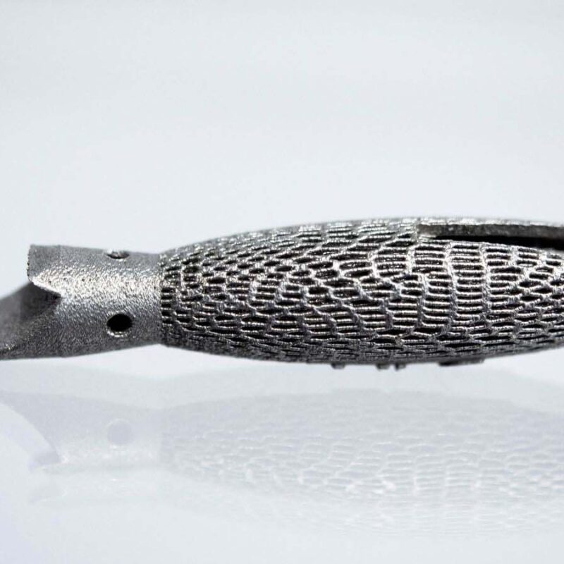 A close-up image of a metallic object with a textured surface and a curved, split tip, possibly a component or tool, displayed on a reflective surface.