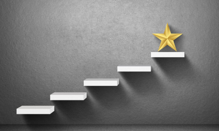 A gray wall with a set of white ascending steps displays a golden star on the topmost step.