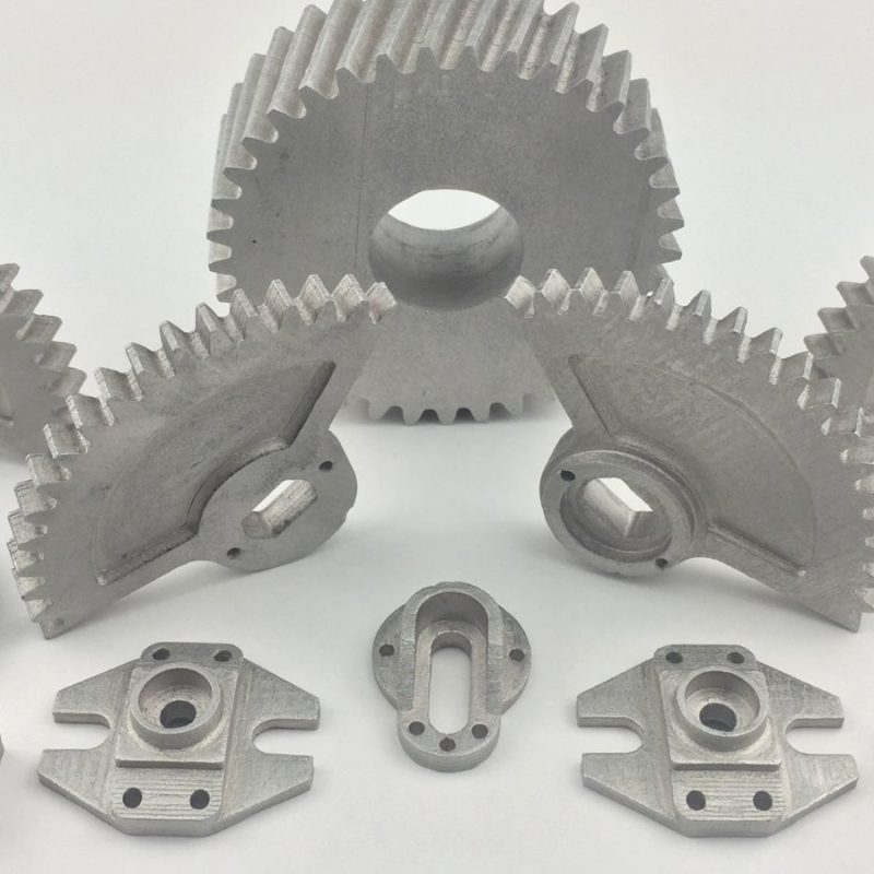 A collection of various metal mechanical components, including gears, brackets, and other precision parts, displayed on a white background.