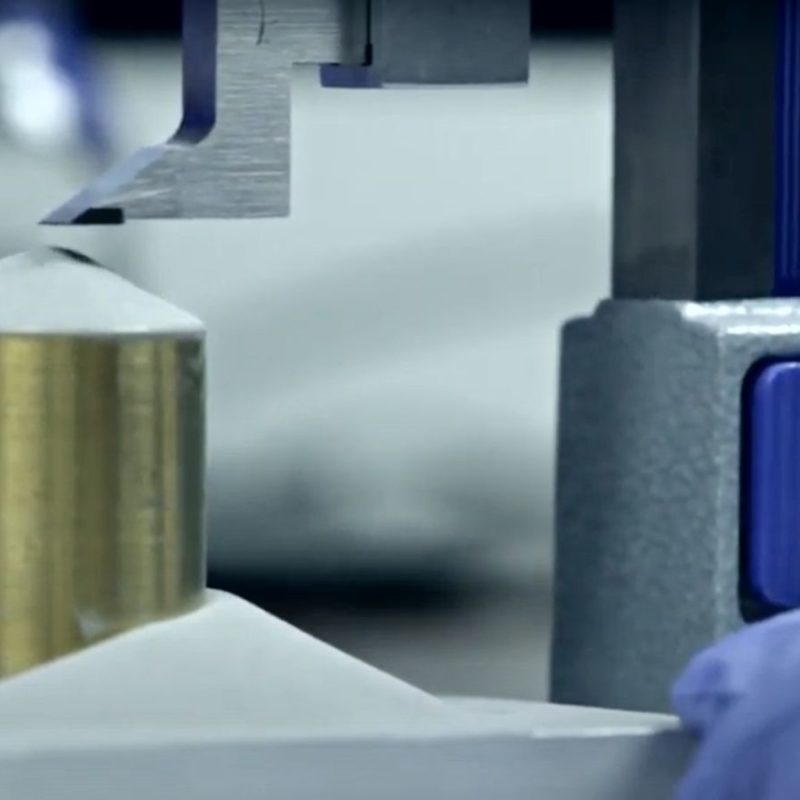 A metal cylinder being tested for pressure resistance in a laboratory setting with a machine applying force from above.