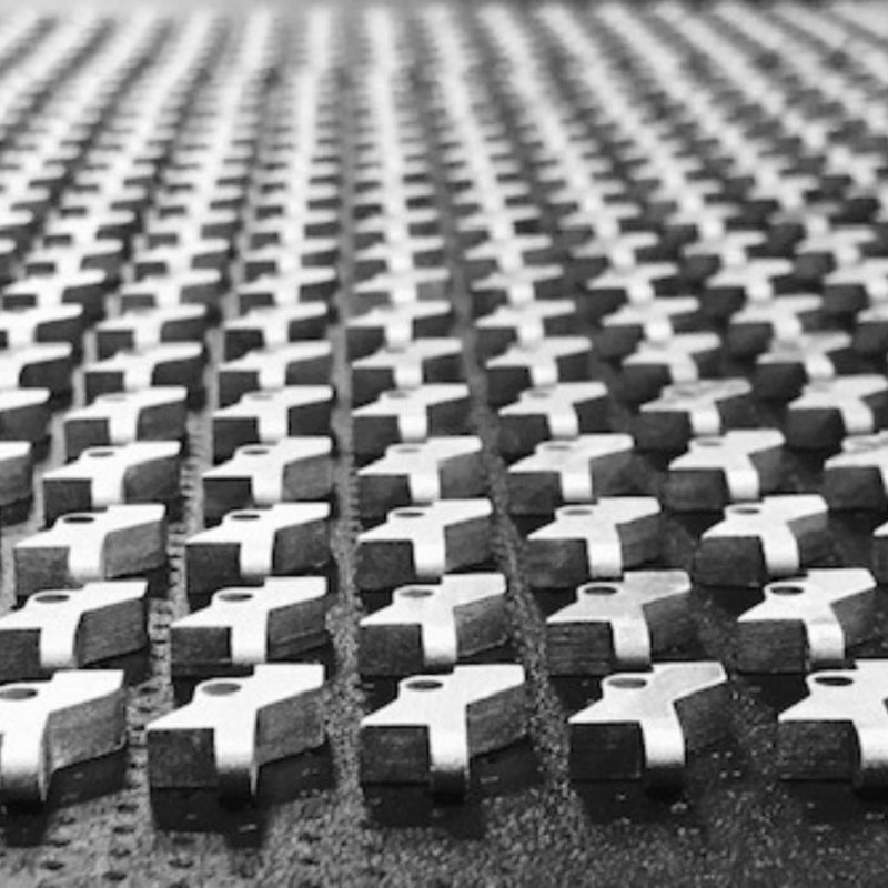 Black and white image of a repetitive pattern of metal crosses arranged in neat rows on a textured surface.
