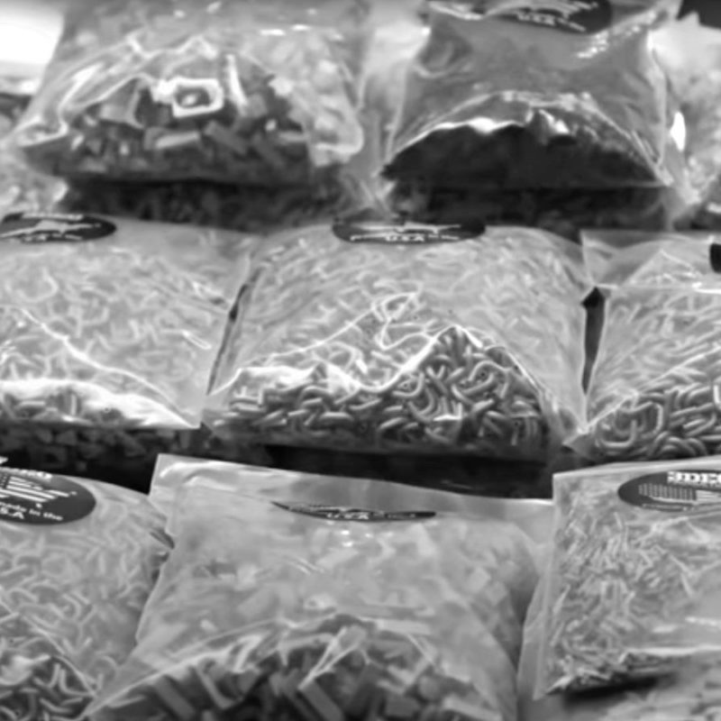 Black and white image of several transparent bags filled with various types of pasta on a table.