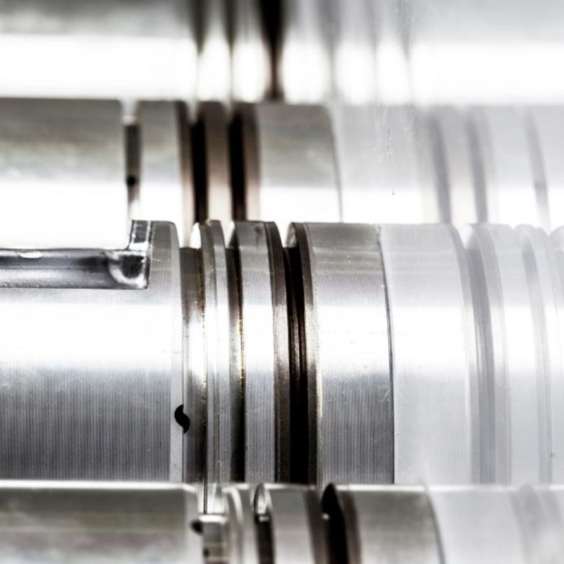 Close-up view of polished cylindrical metal components with precision grooves and cuts, arranged in parallel alignment.