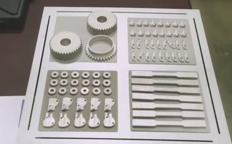 Various 3d-printed mechanical parts displayed on a table, including gears, brackets, and multiple component sets.