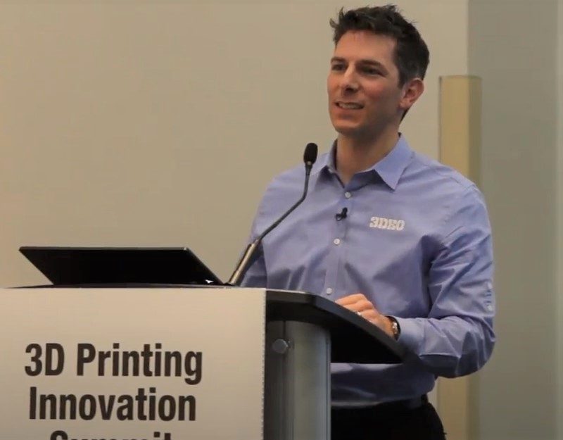A man in a blue shirt speaking at a podium labeled "3d printing innovation summit.