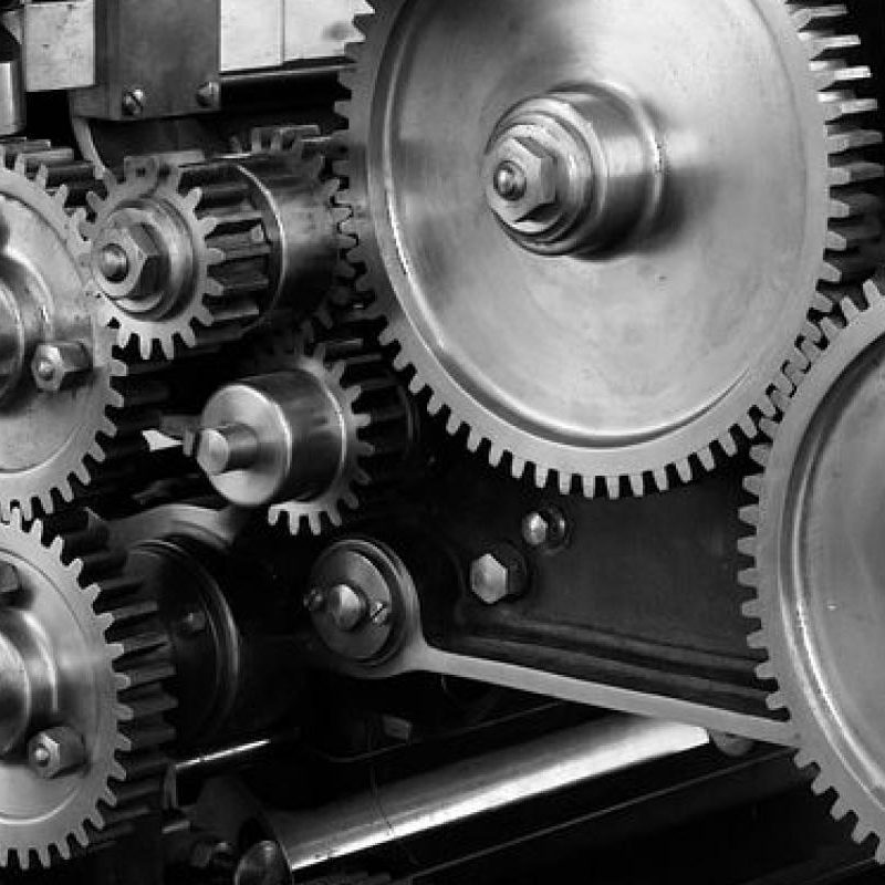 Black and white photo of interlocking metal gears and cogs, showcasing intricate mechanical details.