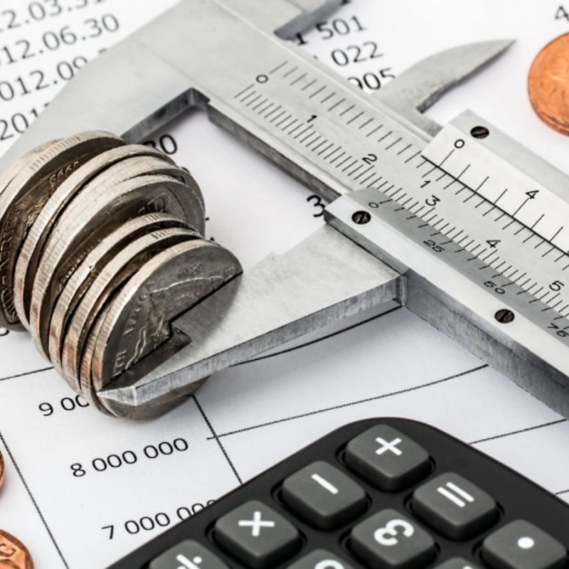 A caliper measures a stack of coins on a financial document, surrounded by additional coins and a calculator.