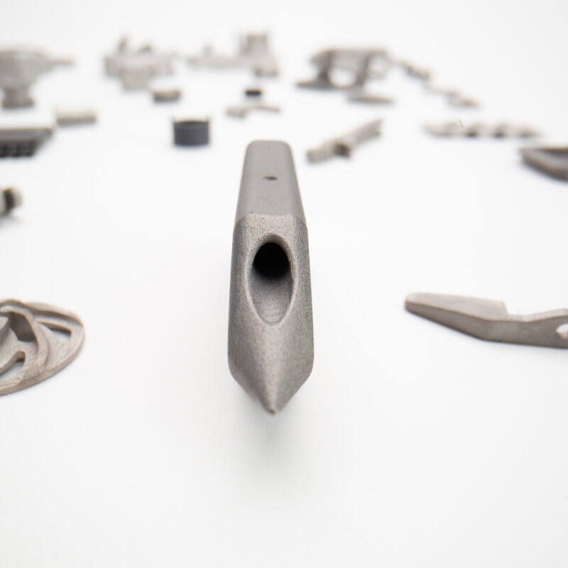 Close-up of a metal object with a hollow center in the foreground, surrounded by various blurred metal components scattered on a white background.