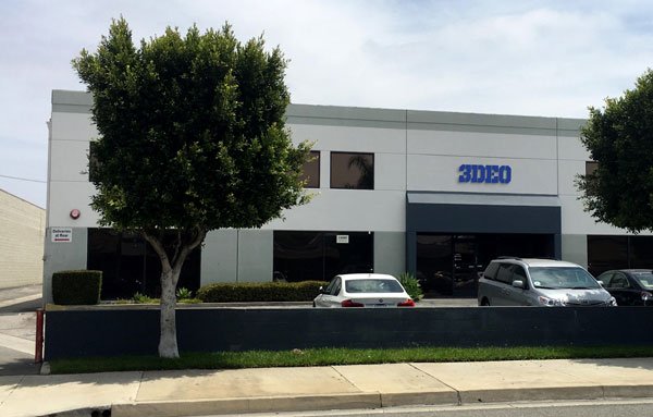 Exterior view of a one-story building with the "3deo" sign, featuring a few parked cars and trees in front of it, specializing in metal 3d printing services, located on a