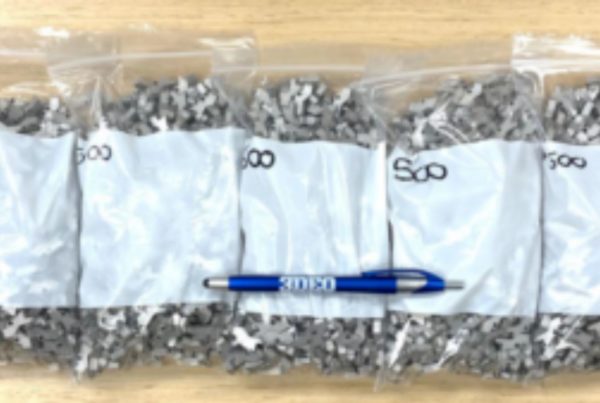 Five plastic bags filled with gray puzzle pieces labeled "500" are lined up on a wooden surface. A blue and silver pen is placed horizontally in front of the bags.