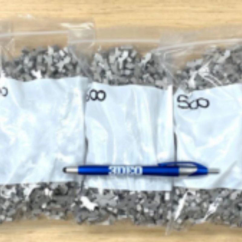 Five plastic bags filled with gray puzzle pieces labeled "500" are lined up on a wooden surface. A blue and silver pen is placed horizontally in front of the bags.