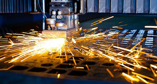 An industrial machine cutting a metal component, emitting bright sparks across a metal grid surface.