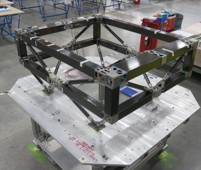 Metallic industrial frame prototype created by a 3D metal printer on a worktable in a workshop, featuring various tools and components in the background.