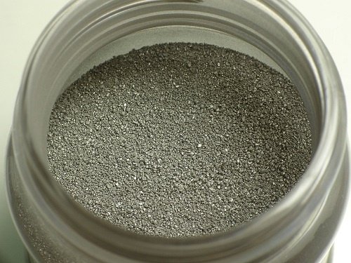 Close-up view of fine, dark gray metallic powder contained in an open jar.