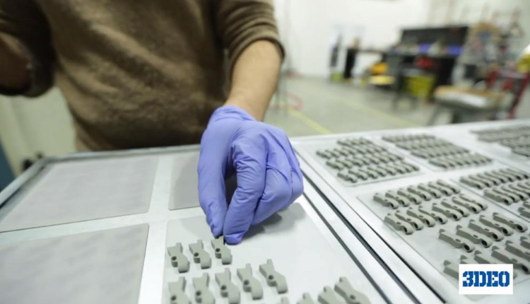 A person wearing blue gloves inspects small metal parts arranged on a tray in a workshop.