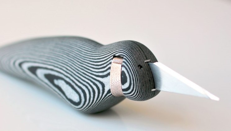 A close-up of a stylized bird sculpture made from layered black and white material using 3D printing, featuring a pointed white beak.