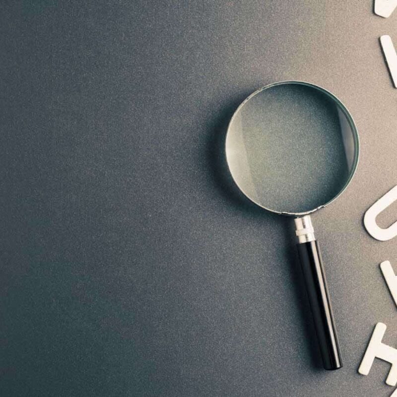 A magnifying glass lies on a dark surface next to scattered white alphabet letters, resembling a meticulous engineer's desk scattered with essential engineering terms.