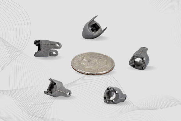 Five small metal 3D-printed parts, including a stainless steel clevis, are displayed around a quarter for size comparison. The background features a light, abstract wave pattern.