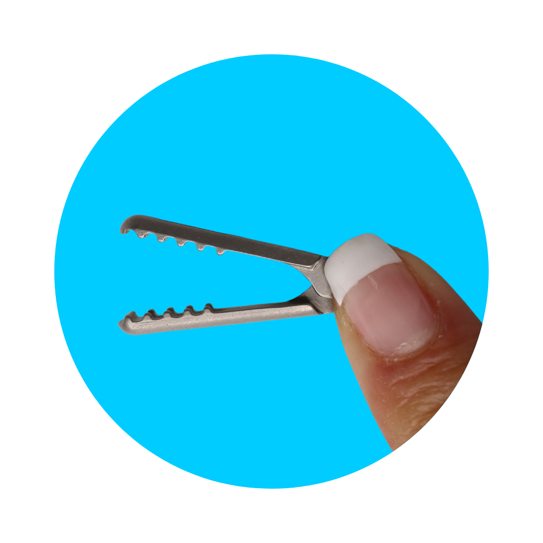 A finger holding miniature surgical tongs against a blue background.
