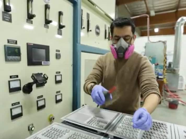 Person wearing protective gear and gloves works with control panels and equipment in an industrial setting.