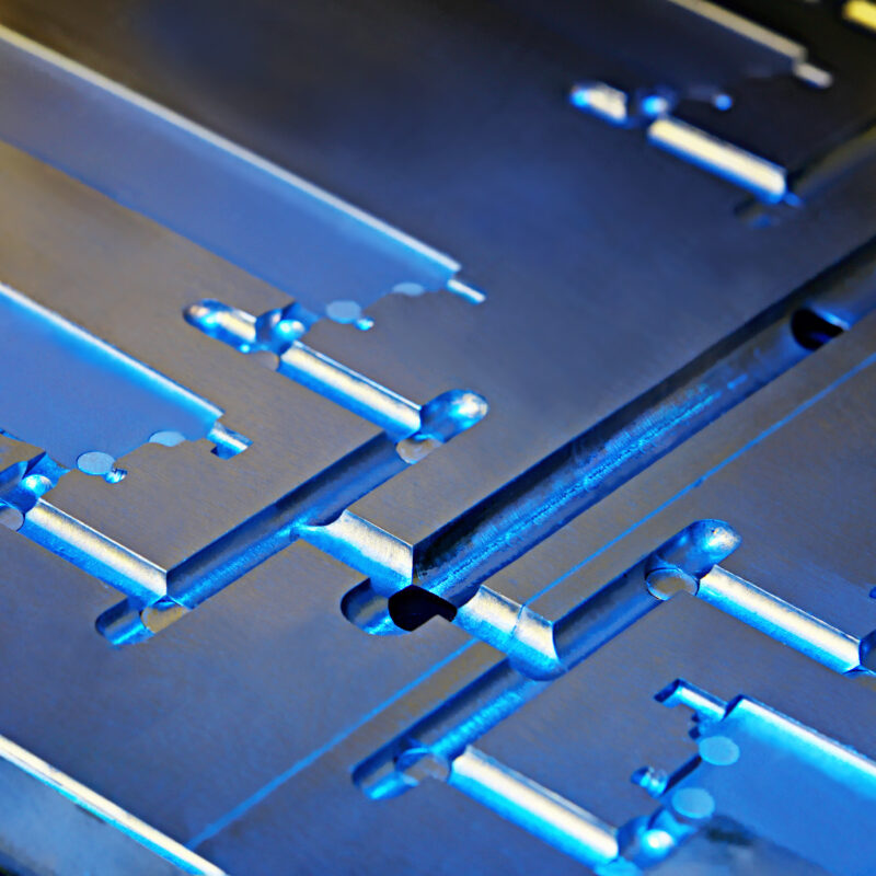 Close-up of a metallic, industrial component with complex geometric shapes and a blue tint, crafted using MIM technology.