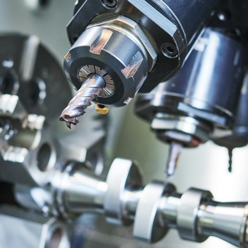 Close-up of a CNC machine with a drill bit poised over a metal workpiece that isn't able to create thin walls, internal channels or hidden geometry like Additive Manufacturing can.