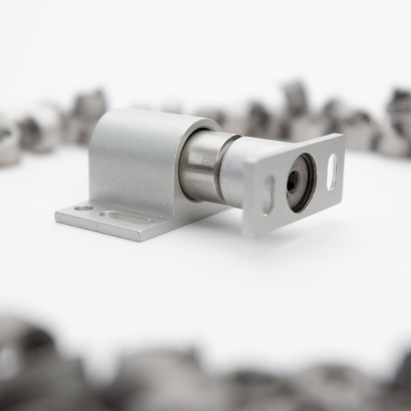 Metal sliding door roller hardware on a white surface, surrounded by blurred metal coils in the background, showcasing the ingenuity of US based manufacturing.